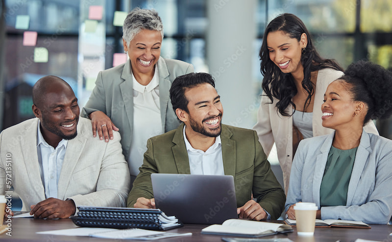 a diverse group of professionals smiling at a conference table, around a laptop, papers, and a coffee cup