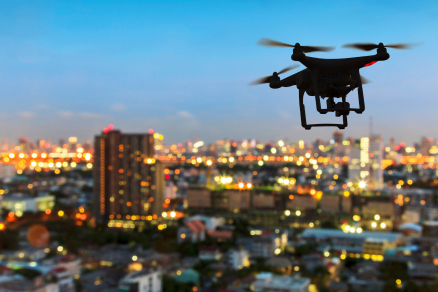 silhouette of drone above city skyline at sunset