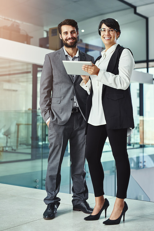 two professionals standing and smiling, one holding a tablet